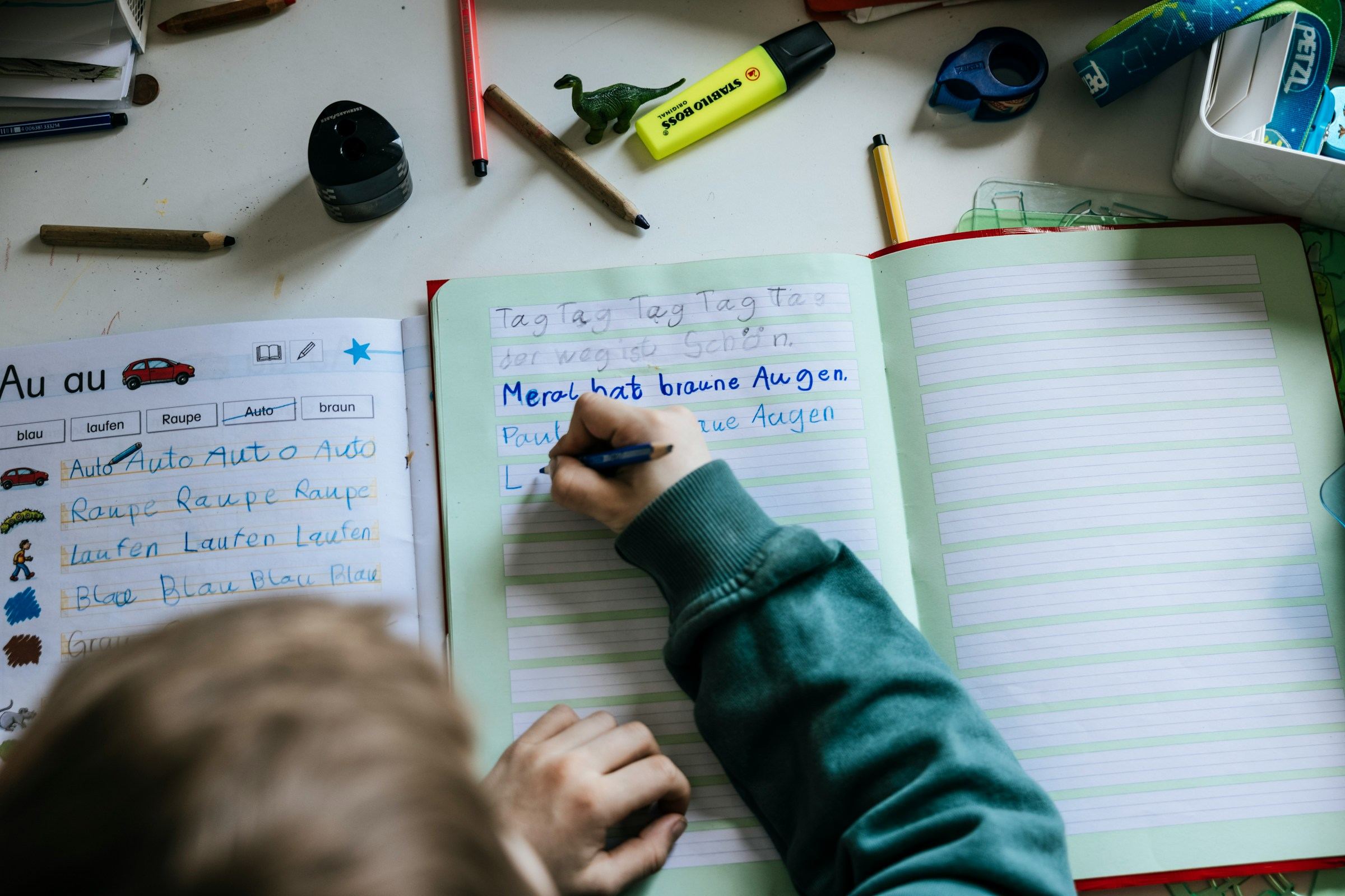 Bambino che scrive su un quaderno a bande colorate, con evidenziatori e matite sul tavolo